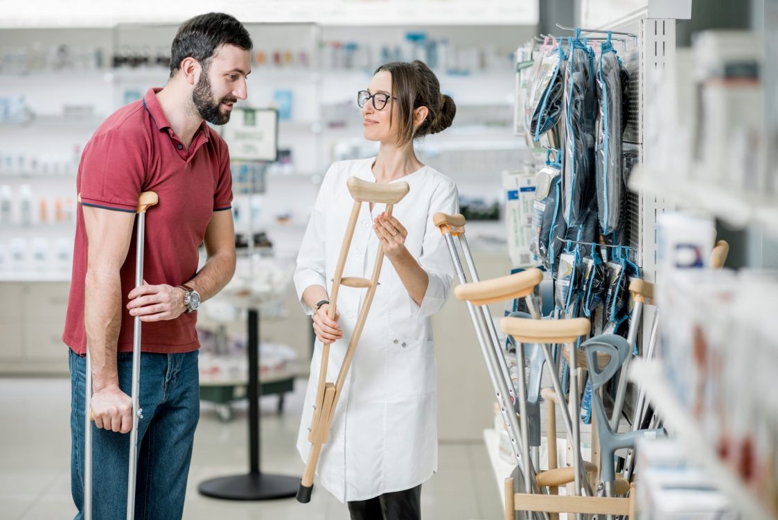 Man choosing crutches in the pharmacy Young woman pharmacist helping to choose crutches for the man in the pharmacy supermarket